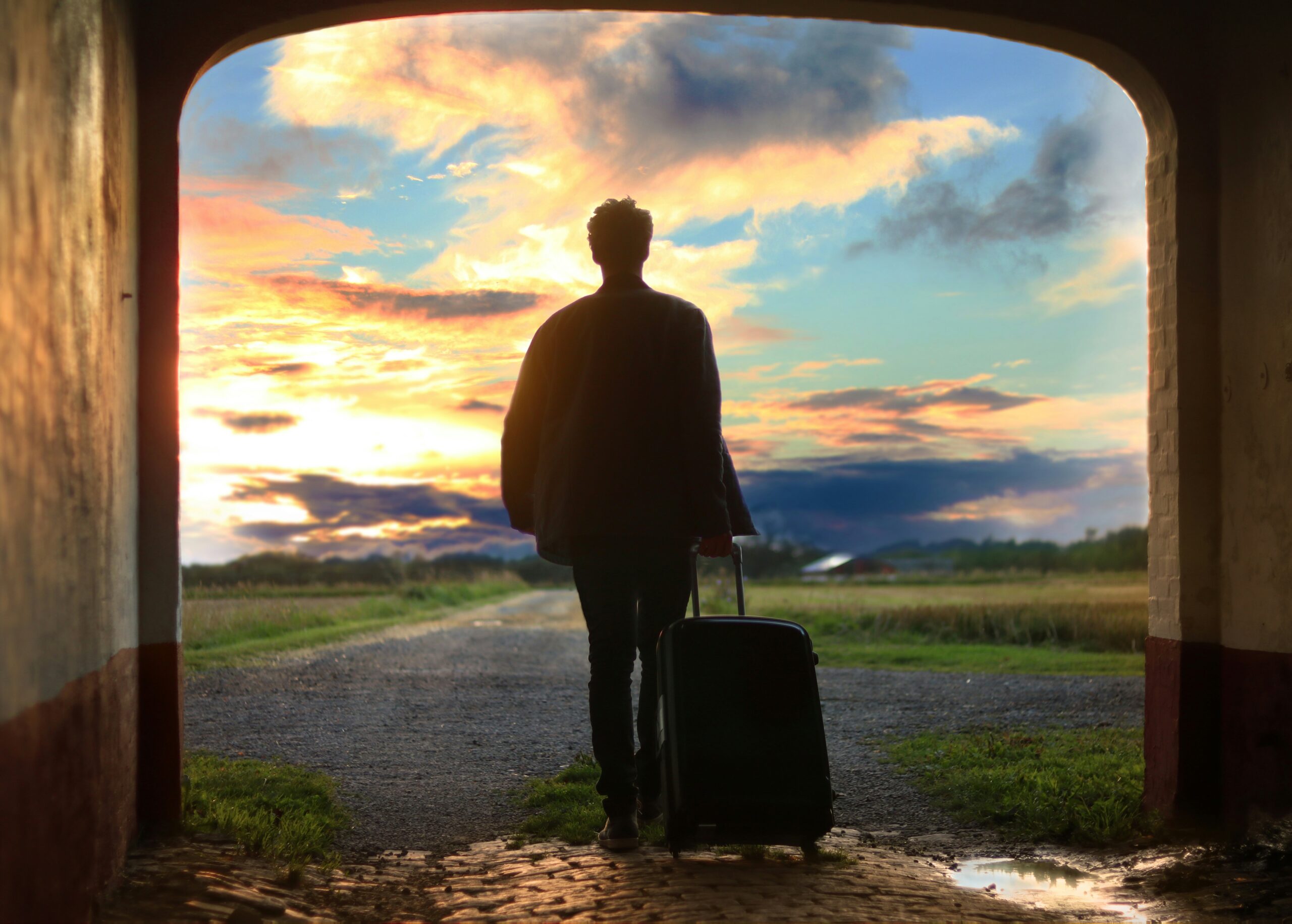 Traveler pulling a suitcase toward an open landscape at sunset
